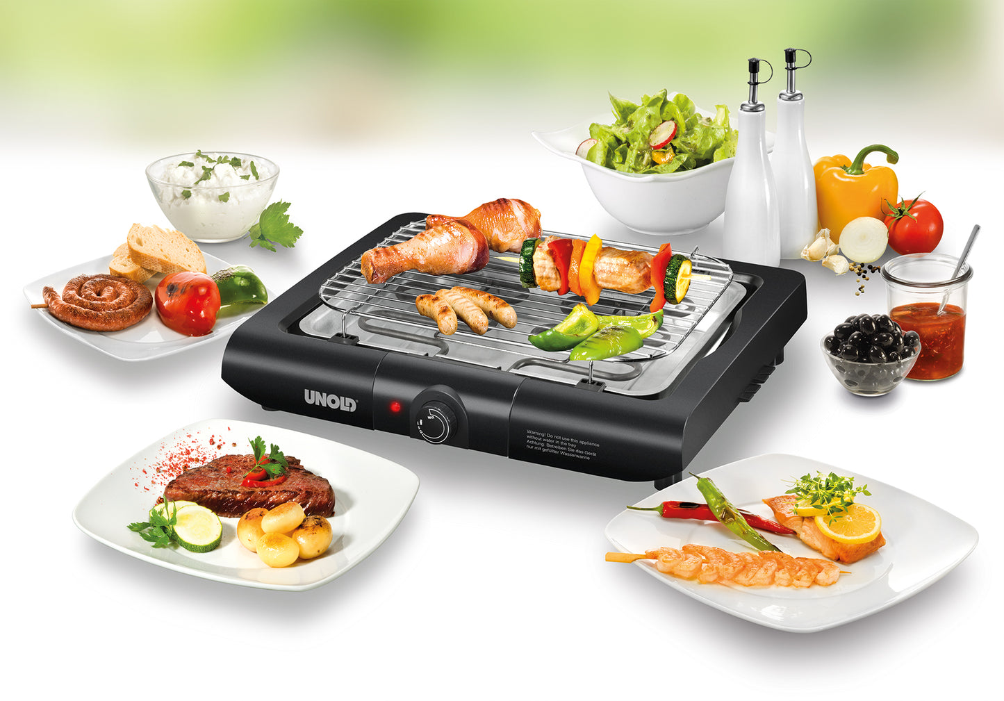 Auf dem Unold Barbecue-Grill Black Rack werden verschiedene Fleischsorten und Gemüse gegrillt, umgeben von Tellern mit Salat, Brot, Grillgut, Gemüse, Soßen und Gewürzen auf einem weißen Tisch.