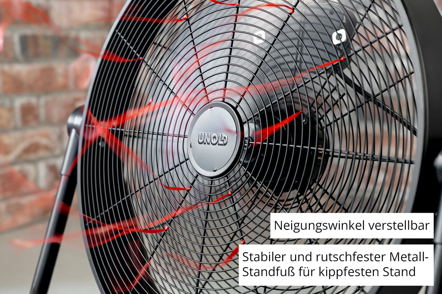 Nahaufnahme des Unold Windmaschine Black Steel Standventilators mit roten Luftstromlinien, verstellbarer Neigung und einem stabilen, rutschfesten Metallsockel. Vor dem Hintergrund einer Backsteinmauer.