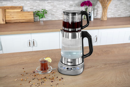 Der Unold AG Samowar Selin, ein Tischteezubereiter mit einer Glaskanne auf dem Wasserkessel, steht auf einem Holztisch neben einem Glas Tee, garniert mit Zitrone und losen Teeblättern.