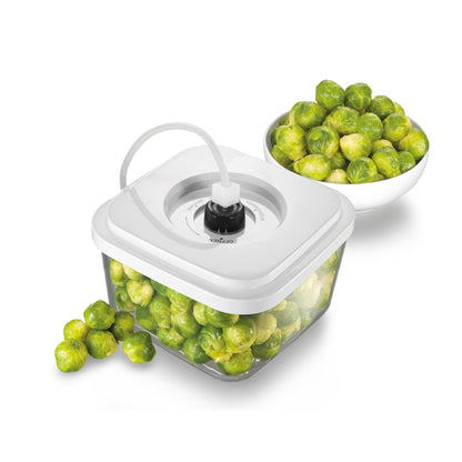 Ein mit Rosenkohl gefüllter, vakuumversiegelter Glasbehälter von Unold Vakuumdose ist an eine weiße Vakuumpumpe angeschlossen. Daneben steht eine weiße Schüssel mit Rosenkohl, daneben liegen einige lose Rosenkohlblätter.