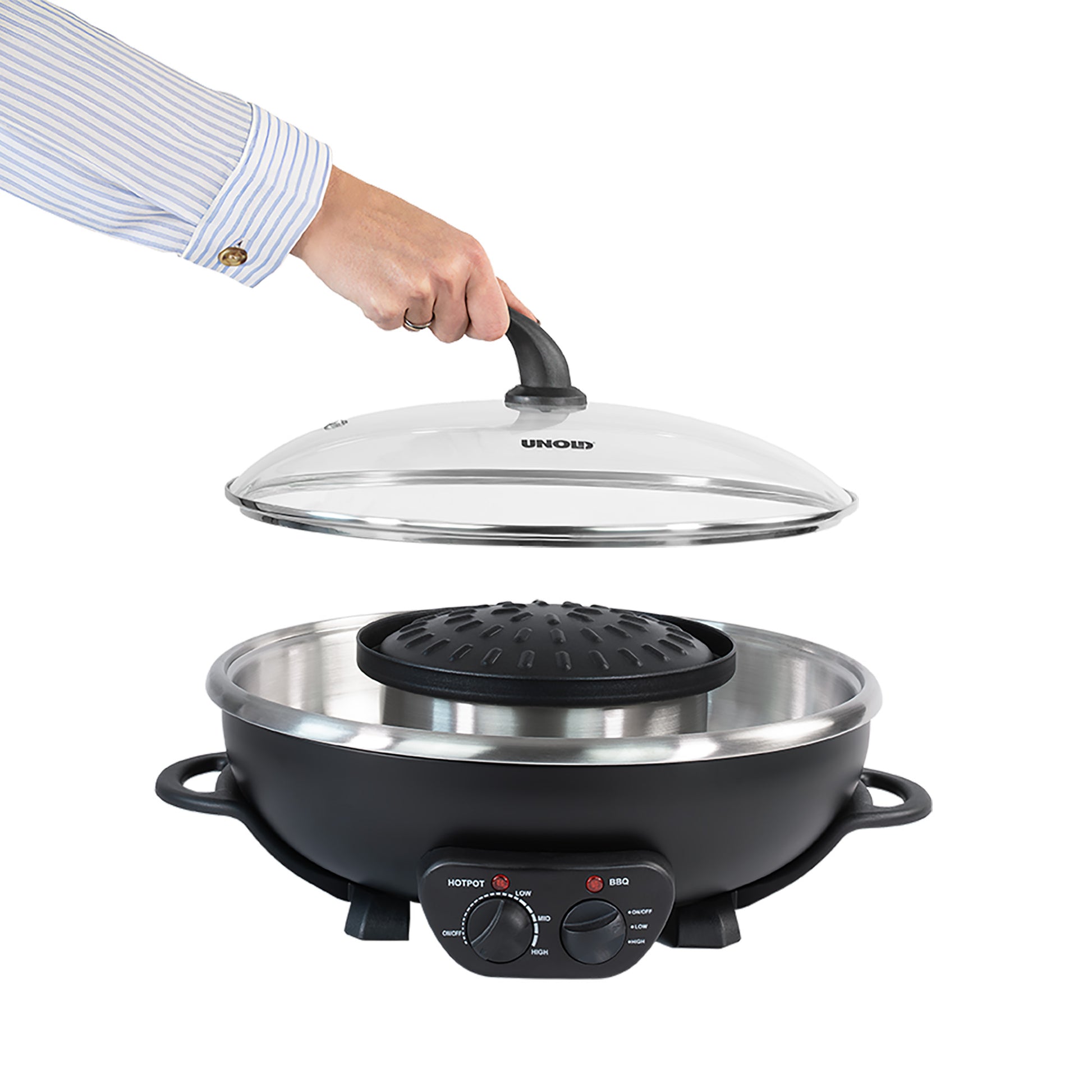 Eine Hand hebt den Glasdeckel vom „Unold Asia Fondue Hot Pot“ ab, einem runden Elektrogrill mit Griffen und Bedienknöpfen an der Vorderseite, der vor einem weißen Hintergrund isoliert abgebildet ist.