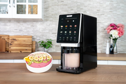 Die Unold AG Eismaschine Cream Dream, ein modernes schwarz-weißes Tischgerät mit digitalem Touchscreen, steht neben einer Smoothie-Bowl mit Banane, Kiwi, Orange und Granola in einer hellen Küche.