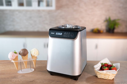 Die Unold Eismaschine Uno 1,2 L steht auf einer hölzernen Küchentheke neben einem Ständer mit drei Eistüten und einem Korb Erdbeeren. Ihre Digitalanzeige zeigt 55:58.