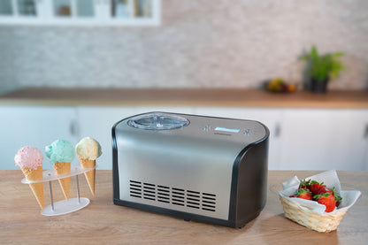 Die Unold Eismaschine One 1,2 L steht auf einer Küchentheke neben einem Ständer mit drei Eistüten und einem Korb mit frischen Erdbeeren vor einem unscharfen Küchenhintergrund.