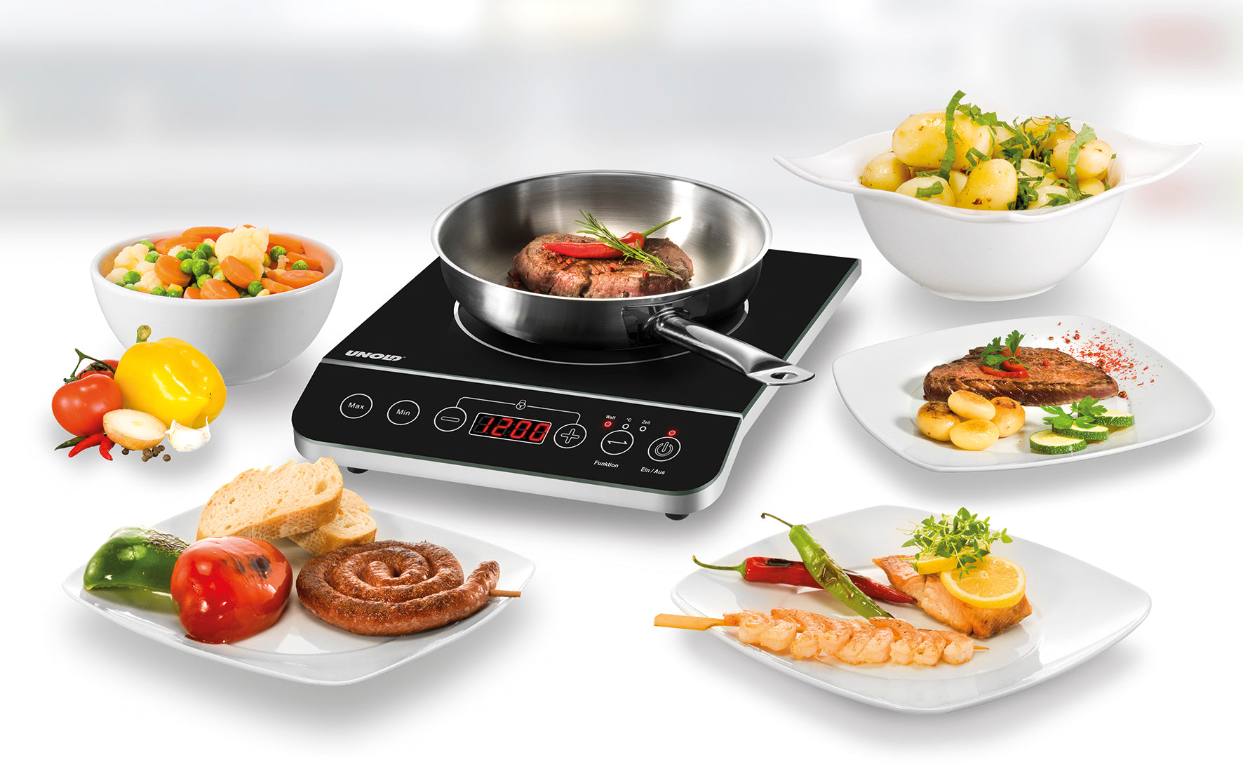 Die Unold Einzel-Induktionskochplatte - Schwarz/Edelstahl 581051 (B-Ware) der Unold AG zeigt ein gebratenes Steak in einer Pfanne, umgeben von gekochtem Gemüse, Kartoffeln, gegrilltem Fleisch, Garnelen, Brot und frischen Produkten auf einer weißen Fläche.