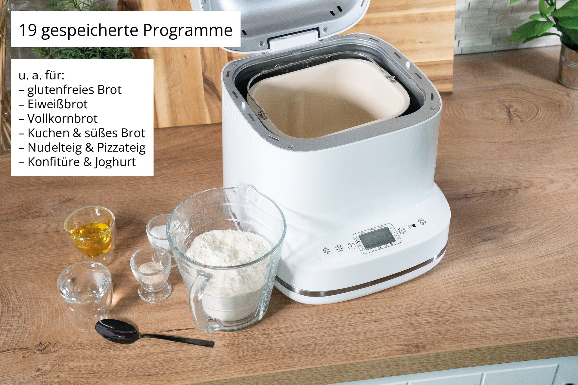Der Brotbackautomat der Unold AG Backmeister Bernd steht offen auf einem Holztisch, umgeben von Mehl, Wasser, Hefe und einem Löffel. Ein Schild weist auf seine 19 voreingestellten Programme für verschiedene Brote und Teige hin.