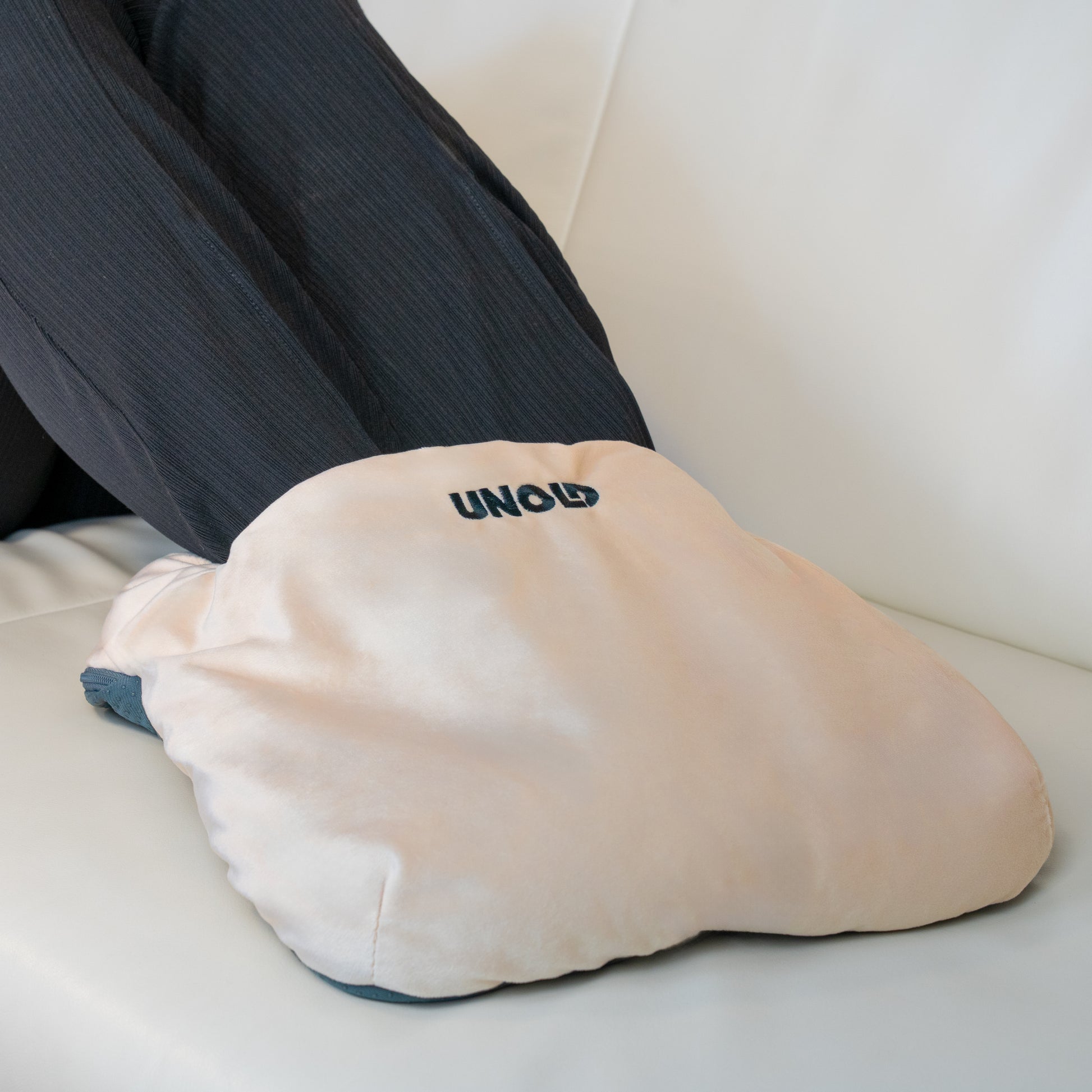 Eine Person entspannt sich auf einer weissen Couch mit den Füssen im beigen Wärmi Premium Set Fusswärmer der Unold AG, auf dem der Markenname aufgedruckt ist.