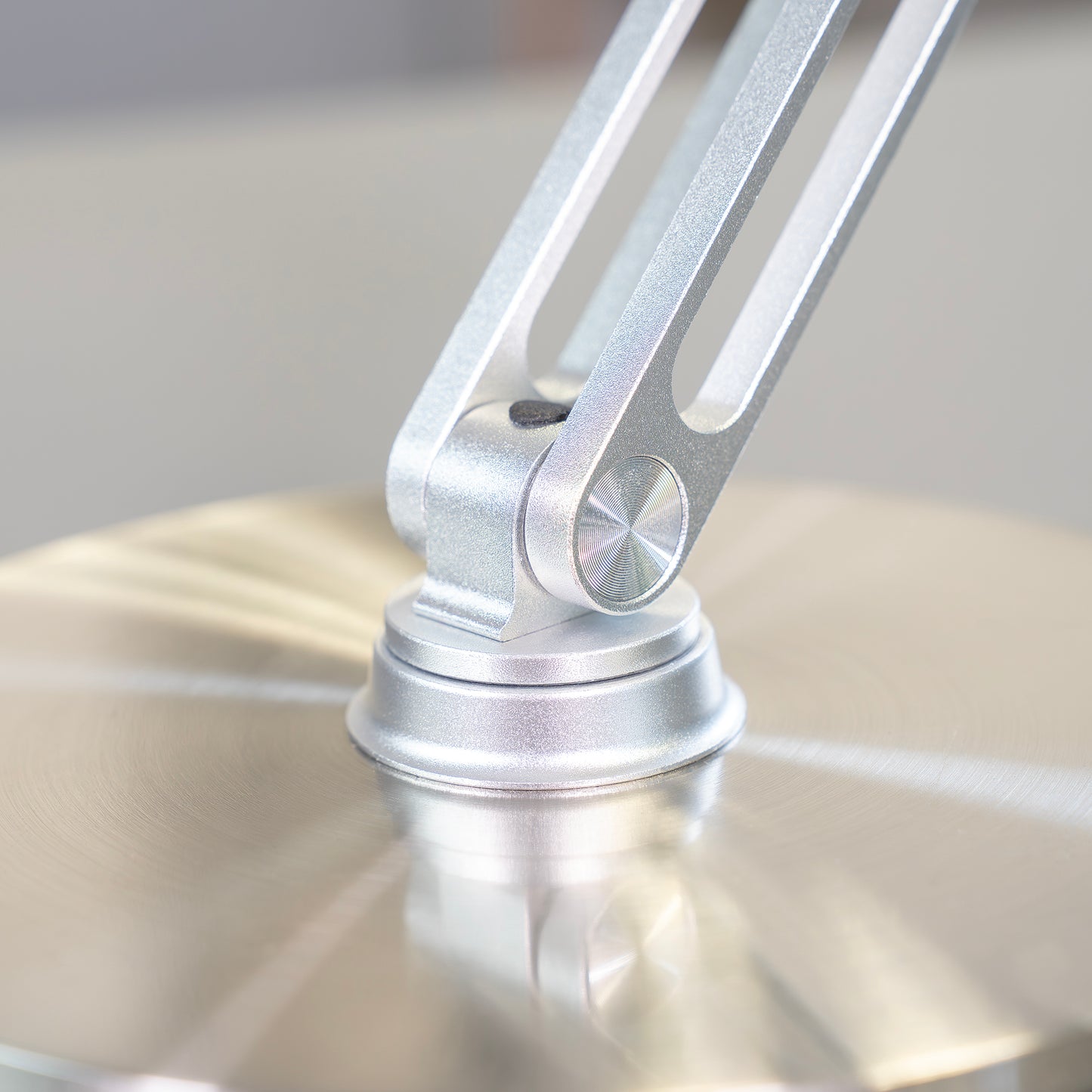 Nahaufnahme des Unold AG Akku-Tischventilators Steel Flex: Ein modernes, metallisches Scharnier mit gebürstetem Finish verbindet den schlanken Arm mit dem runden Sockel in schlichten Silbertönen, unterstrichen durch sanfte Beleuchtung und eine glatte, spiegelnde Oberfläche.