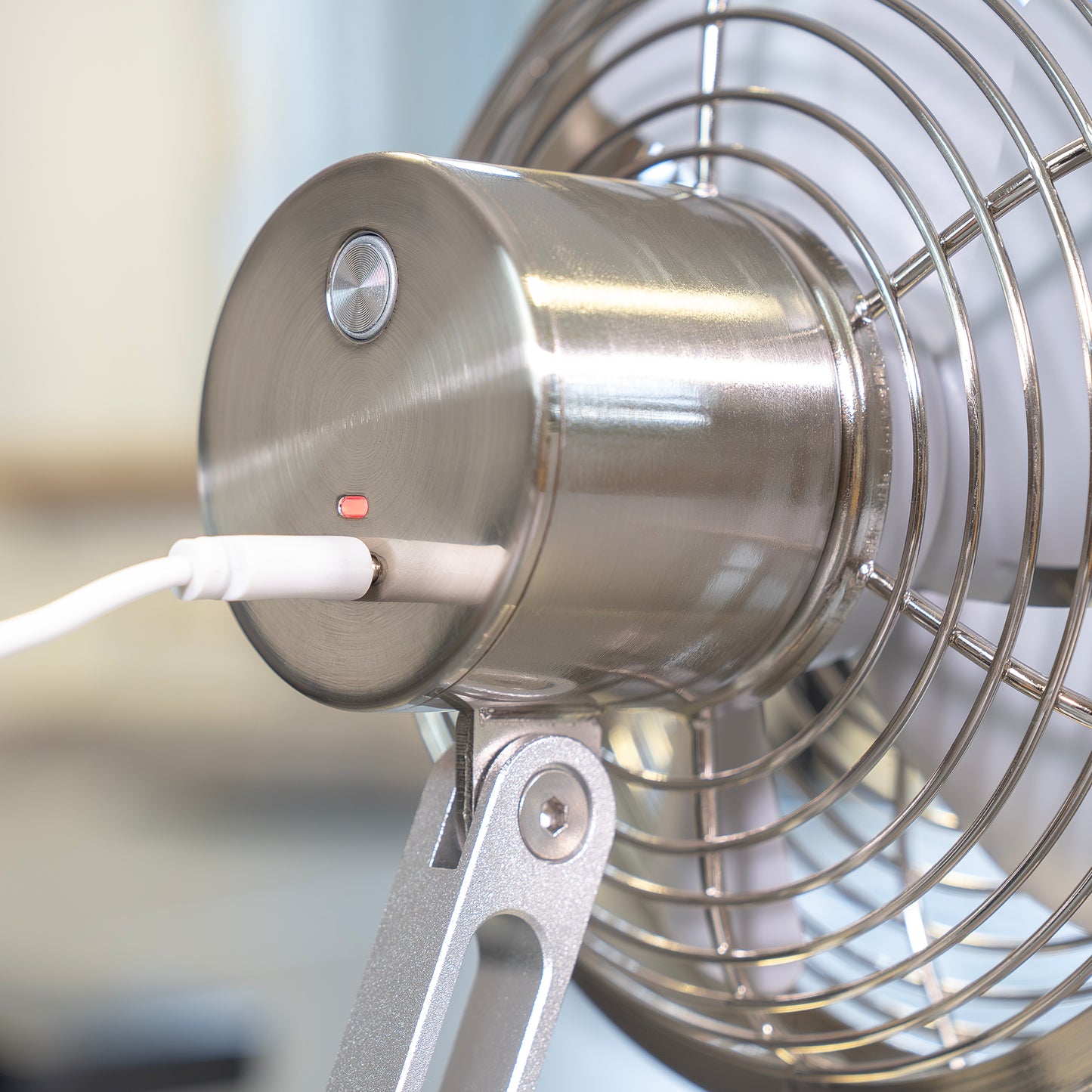Die Nahaufnahme der Rückseite des Unold AG Akku-Tischventilator Steel Flex zeigt die Einschalttaste, die rote Kontrollleuchte, das weiße Ladekabel und das teilweise sichtbare Stahlgitter.