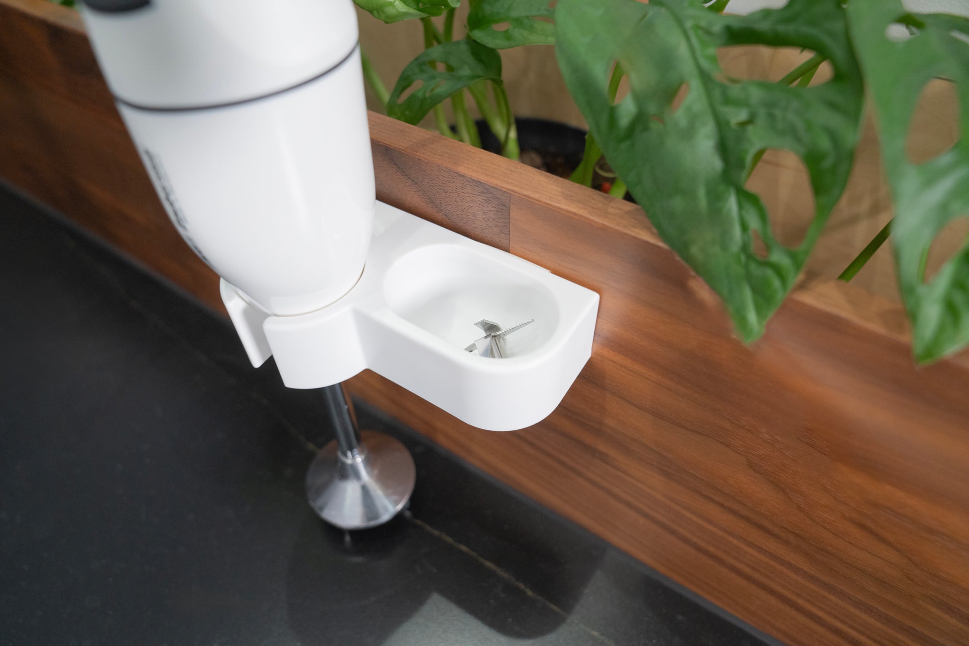 Der Unold ESGE-Zauberstab® M 100 Design Weiß steht auf einer Holztheke neben einer Grünpflanze, der Messeraufsatz ruht in einer kleinen weißen Halterung.