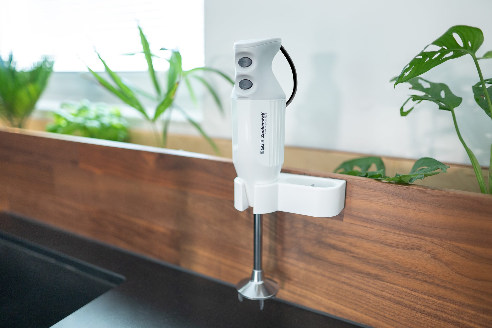 Der Unold ESGE-Zauberstab® M 122 De Luxe steht auf einer hölzernen Arbeitsplatte in einer modernen Küche mit grünen Topfpflanzen und natürlichem Licht, das durch das Fenster fällt.
