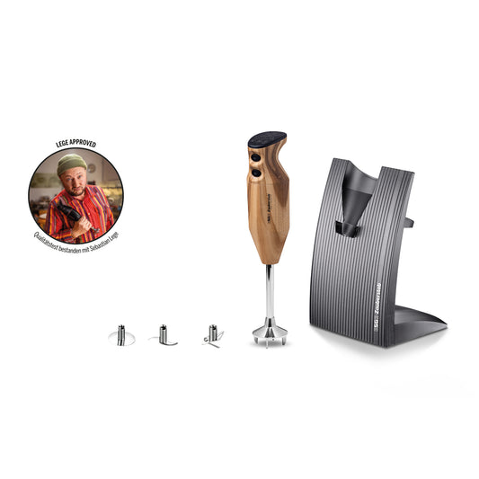 Der ESGE-Zauberstab Design Edition Douglasie, ein Stabmixer von ESGE-Zauberstab, verfügt über einen Holzgriff, wird mit drei Aufsätzen geliefert und umfasst einen stilvollen dunklen Ständer. In einer runden Einlage ist ein Koch zu sehen, der den Daumen hochhält, neben dem Schriftzug „LEE APPROVED“.
