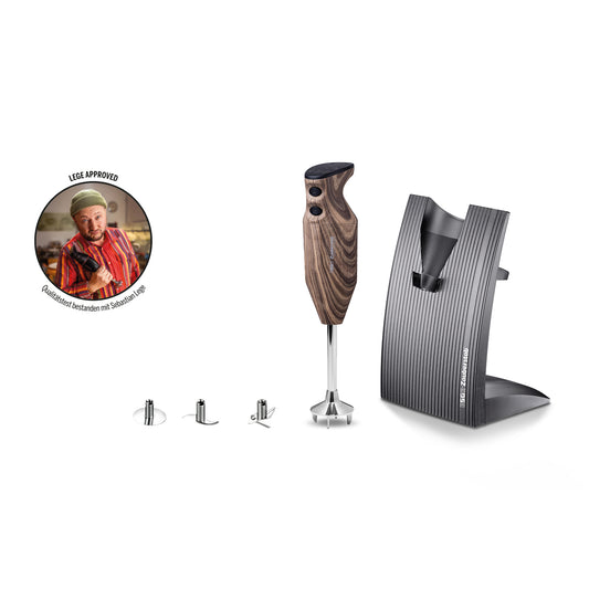 Der Stabmixer „ESGE-Zauberstab Design Edition Nussbaum“ von ESGE-Zauberstab verfügt über einen Holzgriff, wird mit drei Metallaufsätzen geliefert, enthält einen schwarzen Ständer und ist mit einem runden Foto eines Kochs verziert, auf dem der Text „LECK APPROVED“ zu lesen ist.