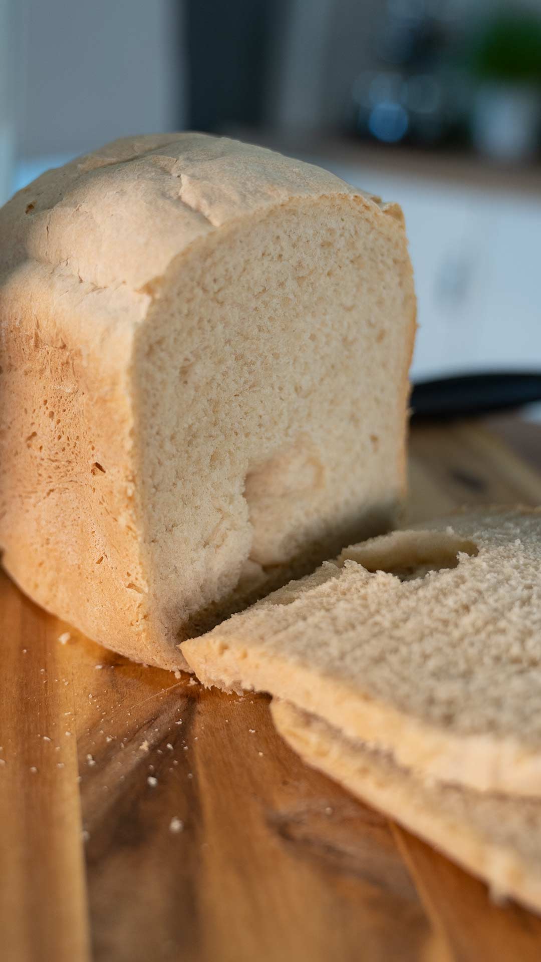 Ein Laib geschnittenes Brot liegt auf einem hölzernen Schneidebrett. Zwei Scheiben sind abgeschnitten und liegen flach vor dem Laib. Auf dem Brett sind Krümel verstreut.