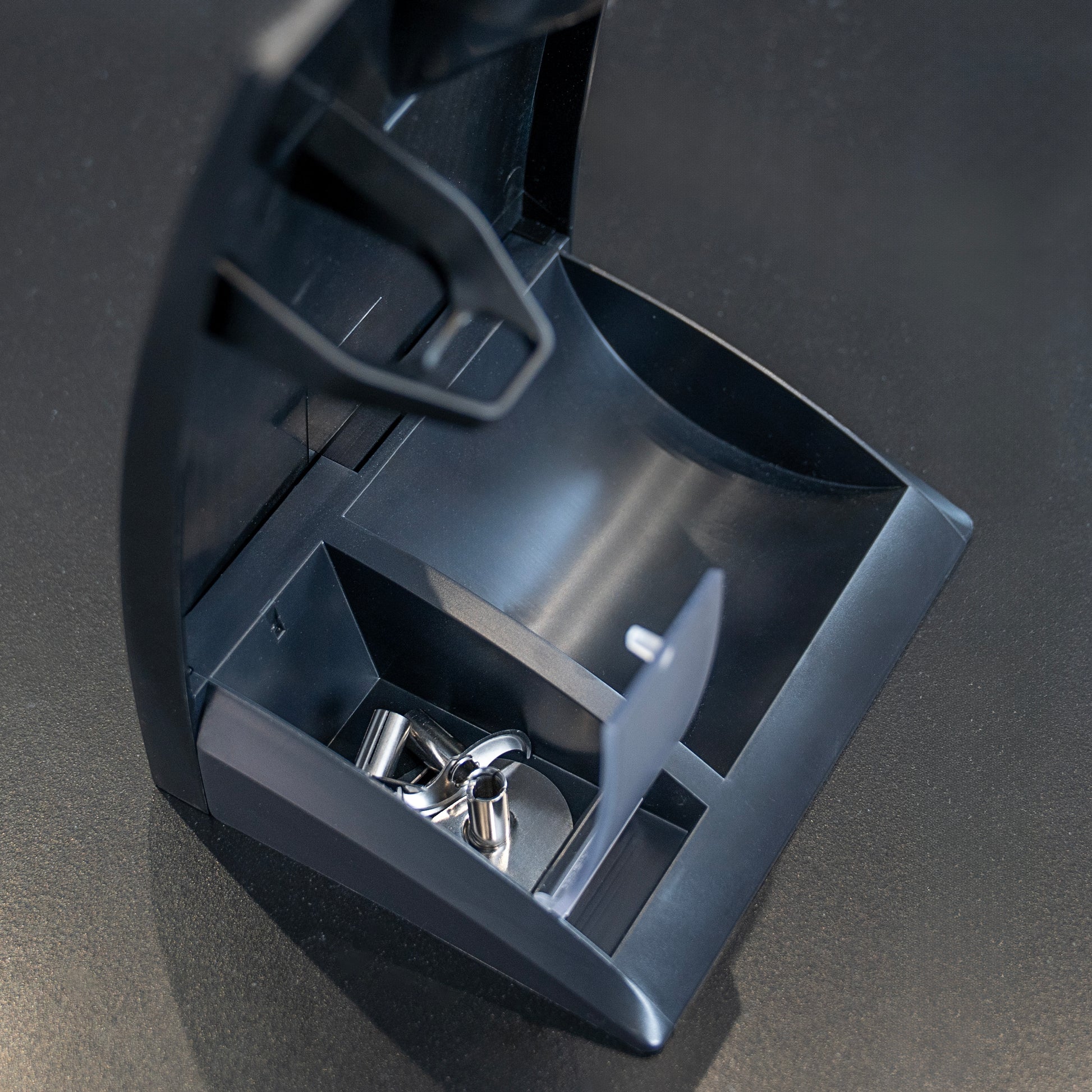 Eine Nahaufnahme der ESGE-Zauberstab Design Edition Nussbaum von ESGE-Zauberstab zeigt mehrere leere Metallkaffeepads in ihrem Behälter für gebrauchte Pads vor einer dunklen Oberfläche.