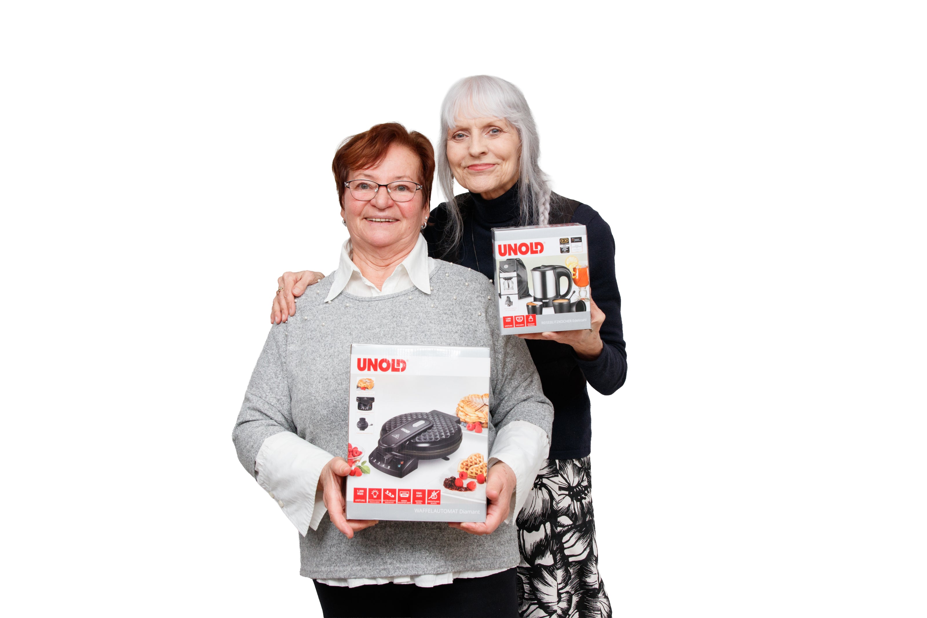 Zwei lächelnde ältere Frauen stehen zusammen und halten verpackte Küchengeräte von UNOLD, eine hält einen Grill und die andere einen Wasserkocher, vor einem schlichten weißen Hintergrund.