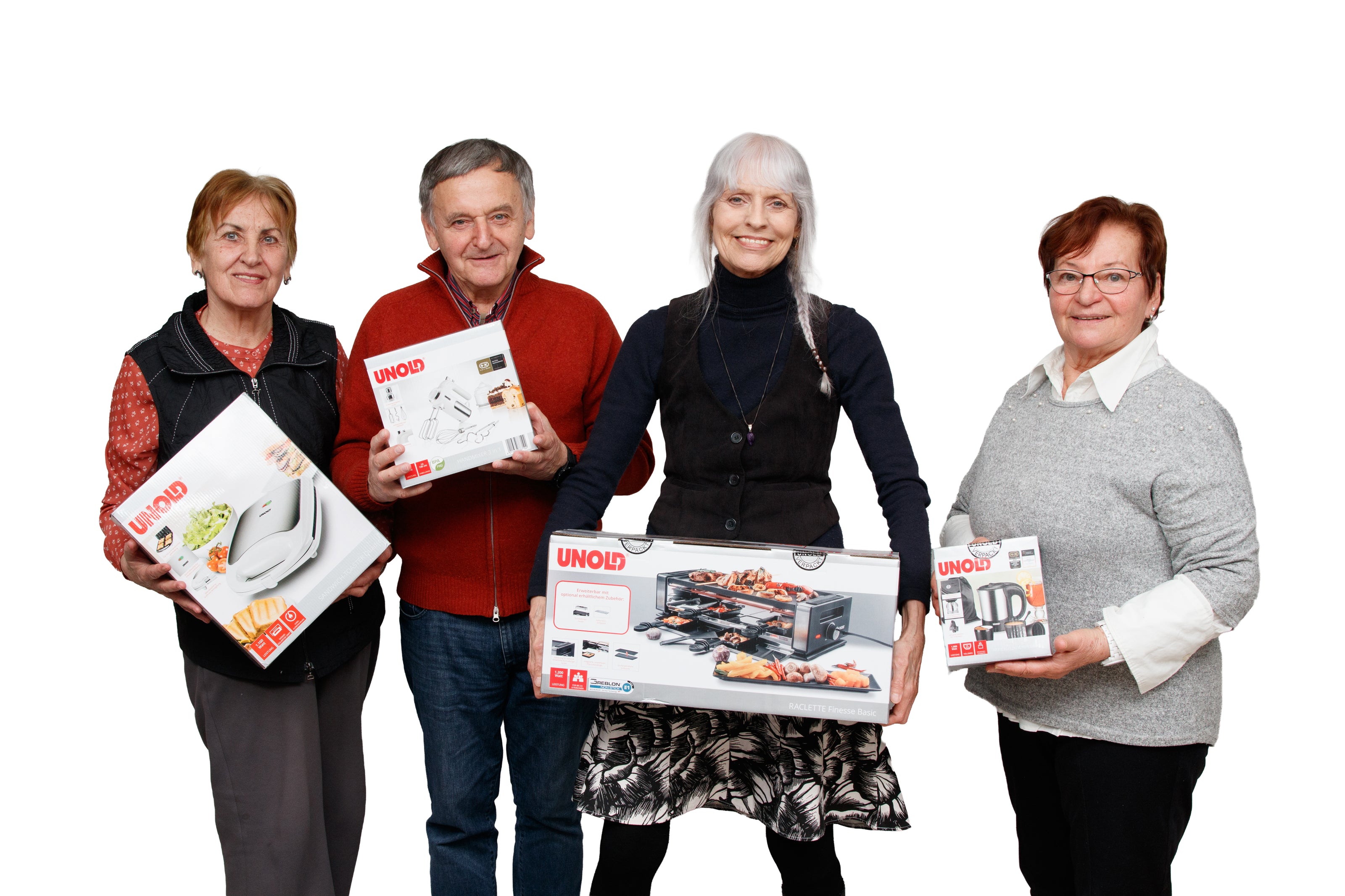 Vier ältere Erwachsene, drei Frauen und ein Mann, stehen lächelnd und mit verschiedenen Küchengeräteboxen in der Hand vor einem weißen Hintergrund. Die Produkte sind von der Marke UNOLD.