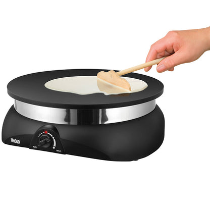 Eine Hand verteilt den Teig mit einem Holzspatel auf dem Unold Crêpesmaker Profi. Der schwarze elektrische Crêpe-Maker verfügt über einen regulierbaren Temperaturregler und steht vor einem weißen Hintergrund.