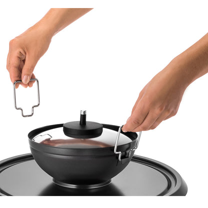 Eine Person hebt mit einem Metallwerkzeug den heißen Deckel sicher vom Unold Raclette Multi 4 in 1 ab und demonstriert so den sicheren Umgang mit dem Kochgeschirr.