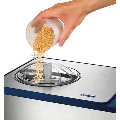 Eine Hand schüttet gehackte Nüsse aus einem Plastikbecher in das offene Fach einer Unold Eismaschine Schuhbeck Exklusiv 1,5 L Eismaschine.