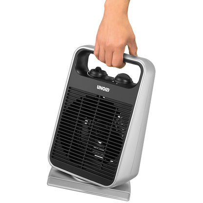 Eine Hand hält den Unold HEIZLÜFTER ROTATE, einen tragbaren rechteckigen Elektroheizer mit silbernem Gehäuse, schwarzem Frontgrill, Bedienknöpfen oben und Unold-Branding über dem Grill.