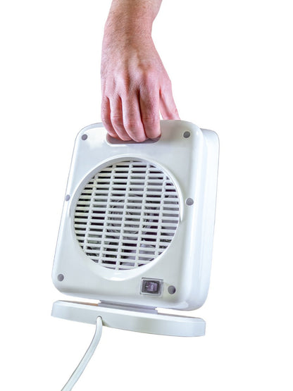 Eine Hand hält den tragbaren, weißen elektrischen Heizlüfter Unold KERAMIK-HEIZLÜFTER IP21 am Griff. Der Heizlüfter verfügt über ein Frontgitter, einen sichtbaren Netzschalter und ein Kabel, das vom Sockel vor einem weißen Hintergrund ausgeht.