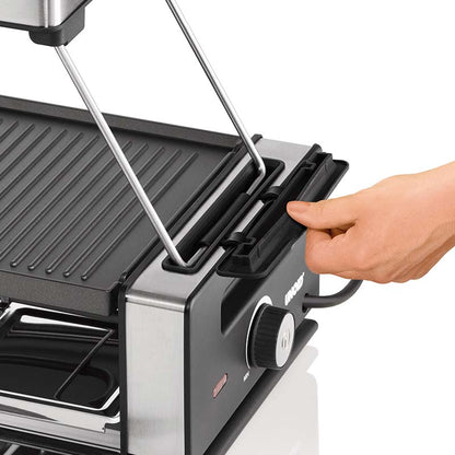 Eine Hand verstellt das Scharnier des rauchfreien Elektrogrills Unold Abzugshaube mit Edelstahlgehäuse, geriffelter Grillfläche, Bedienknopf und Betriebsanzeigeleuchte.